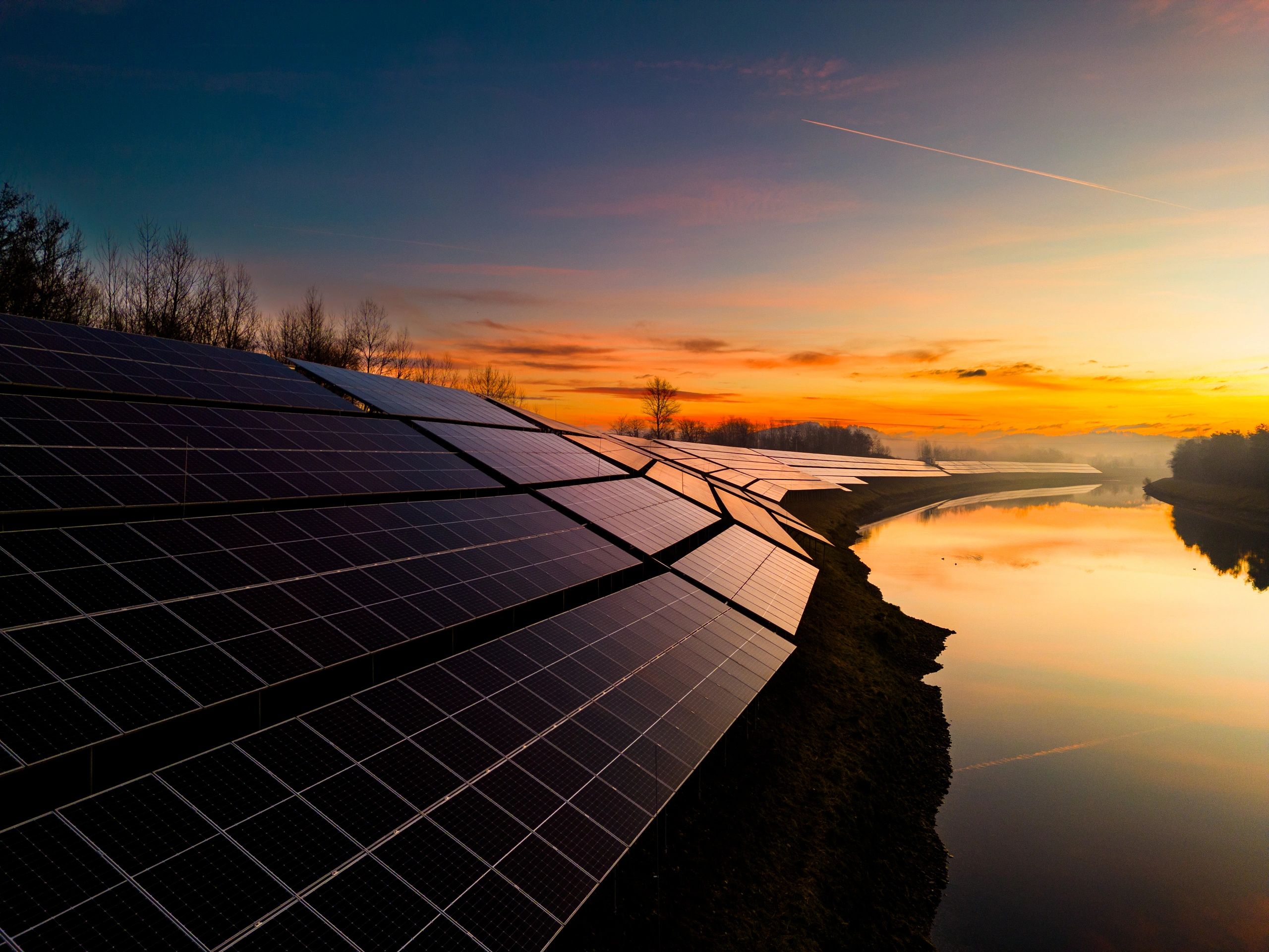 Solar panels by a river at sunset